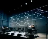 Sur scène, des musiciens jouent devant un écran projetant des schémas lumineux. Une performance pour comment se faire remarquer.