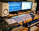Studio d'enregistrement avec deux écrans affichant des pistes audio, des tables de mixage, des enceintes, un clavier MIDI et un microphone. Le fichier midi est prêt à être créé.