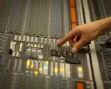 Main d'un ingénieur du son ajustant les faders d'une console de mixage pour un son stéréo parfait.