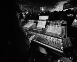 Une personne manipule une console de mixage dans un studio d'enregistrement, devant une foule lors d'un concert.