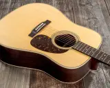 Une guitare acoustique Martin D-28, avec son corps en bois sombre et sa table claire, repose sur un fond de planches de bois grises.