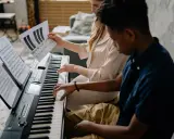Deux jeunes jouent du piano, l'un tenant une partition montrant l'accord D7.