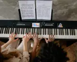 Deux mains jouent un accord c/b piano, des partitions sur le pupitre.