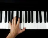 Main gauche jouant le sol 7 piano, doigts effleurant les touches noires et blanches.