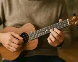 Main d'un musicien jouant un ukulélé, ses doigts formant un nom d'accord guitare sur le manche.