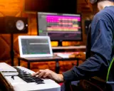 Un musicien utilise un clavier et un ordinateur pour créer une composition musicale. L'application d'accompagnement musical est visible sur les écrans.