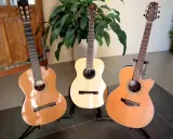 Trois guitares folk nylon, une classique, une électro-acoustique et une autre, se tiennent fièrement sur leurs supports, prêtes à faire vibrer leurs cordes.