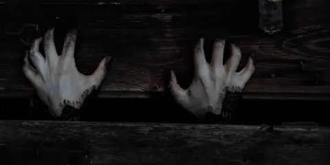 Mains pâles aux doigts noircis sortant d'une caisse en bois sombre, évoquant une musique qui fait peur au piano.