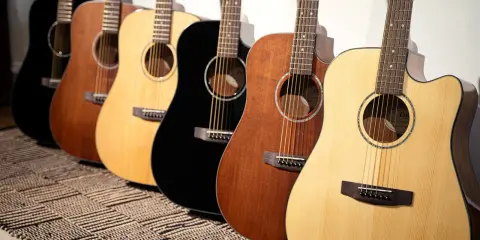 Une rangée de guitares acoustiques Cort, noires, marron et naturelles, posées sur un tapis rayé.