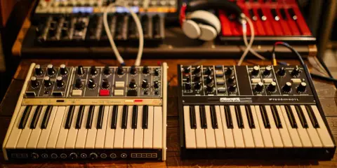 Deux synthétiseurs, l'un blanc et l'autre noir, sont alignés. Leurs claviers et boutons invitent à explorer les mondes analogique et numérique de la musique.