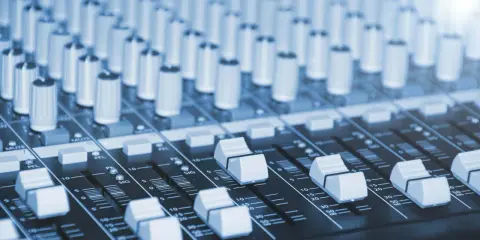 Vue rapprochée d'une console de mixage dans un studio de production musicale, avec ses potentiomètres et faders prêts à sculpter le son.
