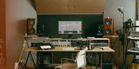 Un studio d'enregistrement avec des enceintes, un ordinateur affichant une station de travail audio numérique, des claviers, une guitare et divers équipements. C'est ici que le producteur de musique crée des sons.