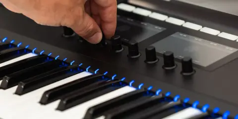 Main d'un musicien ajustant un bouton sur un clavier de musique numérique, avec des touches illuminées de bleu.