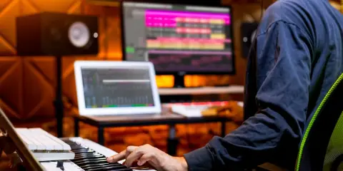 Un musicien utilise un clavier et un ordinateur pour créer une composition musicale. L'application d'accompagnement musical est visible sur les écrans.