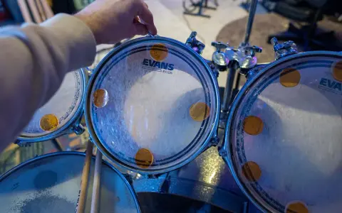 Main d'un batteur ajustant un timbre sur une peau de batterie Evans, prêt à monter une batterie pour un concert.
