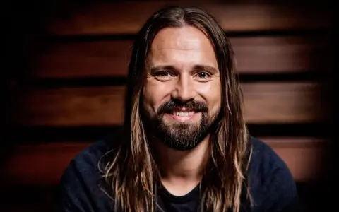 Un homme souriant aux longs cheveux bruns et à la barbe, peut-être un des compagnons d'écriture de Max Martin.
