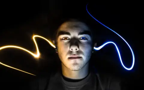 Visage d'un jeune homme éclairé par des traînées de lumière jaune et bleue, évoquant un ia mixage audio créatif.