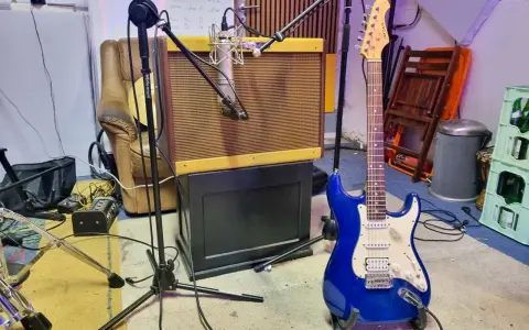 Une guitare électrique bleue étincelante est prête à jouer dans un studio d'enregistrement, à côté d'un ampli vintage et d'un fauteuil usé.