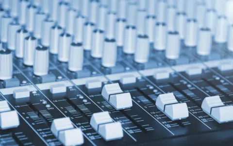 Vue rapprochée d'une console de mixage dans un studio de production musicale, avec ses potentiomètres et faders prêts à sculpter le son.
