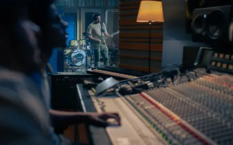 Un guitariste joue dans un studio d'enregistrement, tandis qu'un ingénieur du son est prêt à comment mixer la musique sur la console.