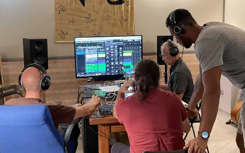 Trois hommes en formation mastering dans un studio d'enregistrement, concentrés sur un écran affichant une console de mixage numérique.
