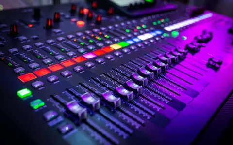 Gros plan sur un **mixer analogique** illuminé par des lumières violettes et rouges. Les faders et les boutons sont prêts pour une session d'enregistrement.