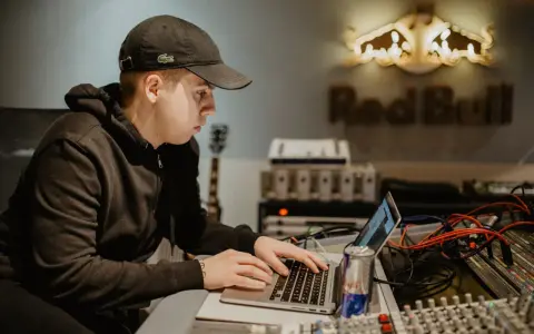Un jeune homme travaille sur un ordinateur portable dans un studio d'enregistrement, avec le logo Red Bull en arrière-plan.