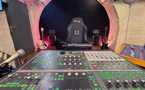 Console de mixage analogique dans un studio d'enregistrement, avec guitares et fauteuil de gamer.