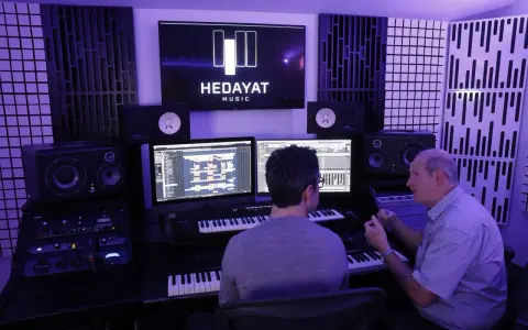 Deux hommes travaillent dans un studio d'enregistrement, le logo HEDAYAT MUSIC est visible sur un écran.