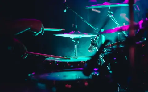 Mains d'un batteur frappant la caisse claire, avec des cymbales illuminées de néons. La **musique accompagnement batterie** crée une ambiance électrique.