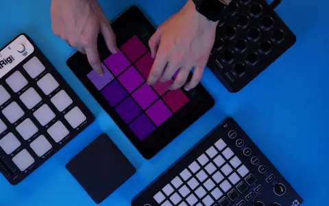 Des mains jouent sur une tablette avec des pads colorés, entourée de contrôleurs pour créer de la musique. Un sampler sans ordinateur en action.