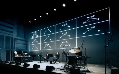 Sur scène, des musiciens jouent devant un écran projetant des schémas lumineux. Une performance pour comment se faire remarquer.