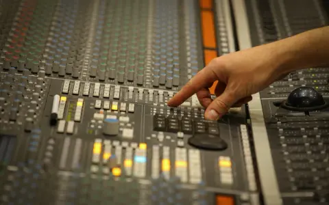 Main d'un ingénieur du son ajustant les faders d'une console de mixage pour un son stéréo parfait.
