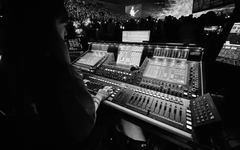 Une personne manipule une console de mixage dans un studio d'enregistrement, devant une foule lors d'un concert.