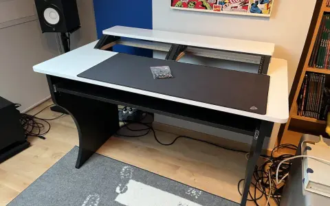Bureau d'angle noir et blanc, prêt pour faire de la musique sur PC. Haut-parleur, tapis de souris et étagères pour équipement audio.