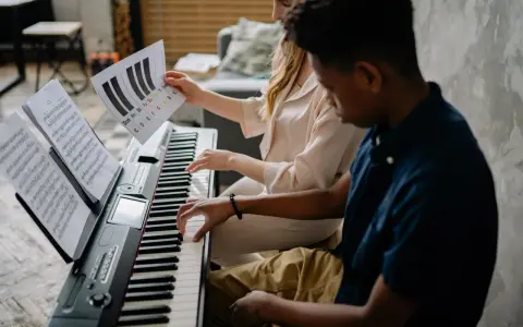 Deux jeunes jouent du piano, l'un tenant une partition montrant l'accord D7.