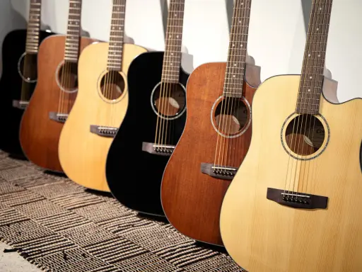 Une rangée de guitares acoustiques Cort, noires, marron et naturelles, posées sur un tapis rayé.