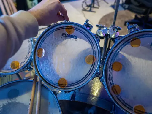 Main d'un batteur ajustant un timbre sur une peau de batterie Evans, prêt à monter une batterie pour un concert.