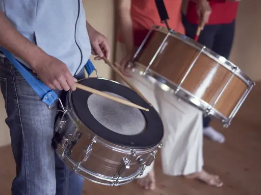 Des musiciens jouent de la percussion brésilienne, leurs mains tenant des baguettes prêtes à frapper les tambours.