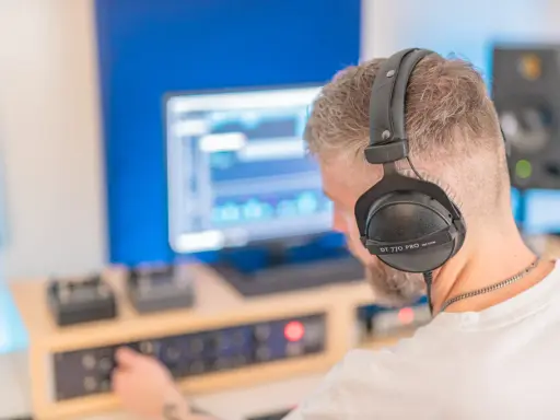 Un homme avec un casque sur les oreilles ajuste les réglages sur une console pour faire un EP dans son studio d'enregistrement.