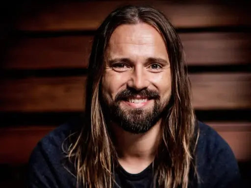 Un homme souriant aux longs cheveux bruns et à la barbe, peut-être un des compagnons d'écriture de Max Martin.