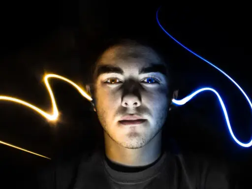 Visage d'un jeune homme éclairé par des traînées de lumière jaune et bleue, évoquant un ia mixage audio créatif.