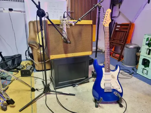 Une guitare électrique bleue étincelante est prête à jouer dans un studio d'enregistrement, à côté d'un ampli vintage et d'un fauteuil usé.