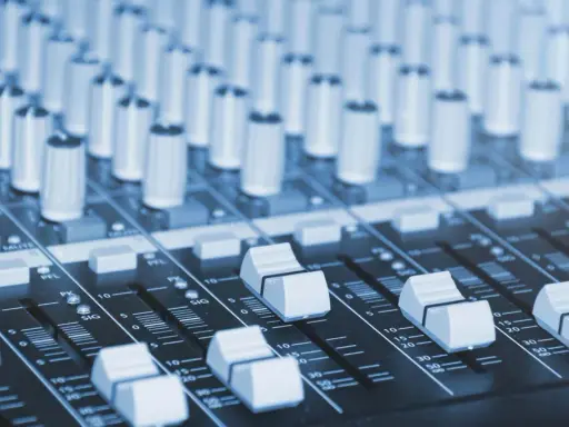 Vue rapprochée d'une console de mixage dans un studio de production musicale, avec ses potentiomètres et faders prêts à sculpter le son.