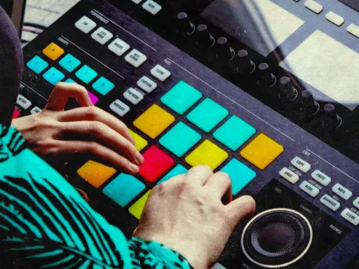 Mains d'un musicien jouant sur un instrument midi coloré, créant des rythmes avec les pads lumineux.