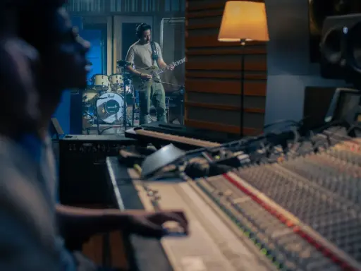 Un guitariste joue dans un studio d'enregistrement, tandis qu'un ingénieur du son est prêt à comment mixer la musique sur la console.
