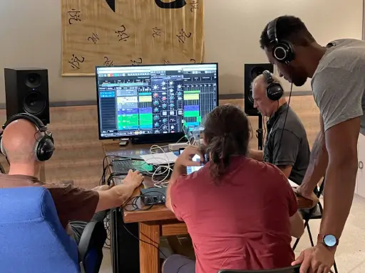 Trois hommes en formation mastering dans un studio d'enregistrement, concentrés sur un écran affichant une console de mixage numérique.