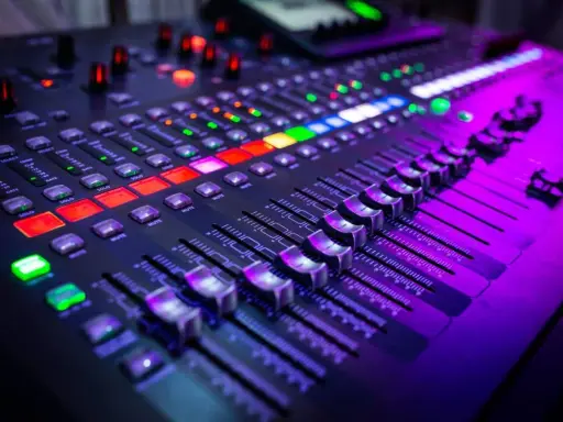 Gros plan sur un **mixer analogique** illuminé par des lumières violettes et rouges. Les faders et les boutons sont prêts pour une session d'enregistrement.