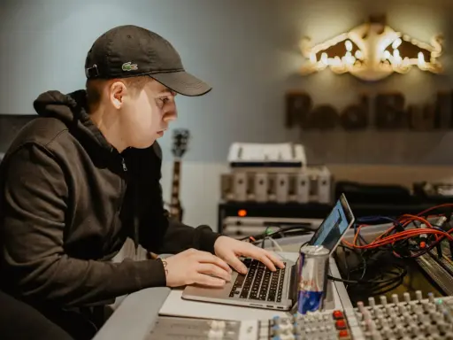 Un jeune homme travaille sur un ordinateur portable dans un studio d'enregistrement, avec le logo Red Bull en arrière-plan.