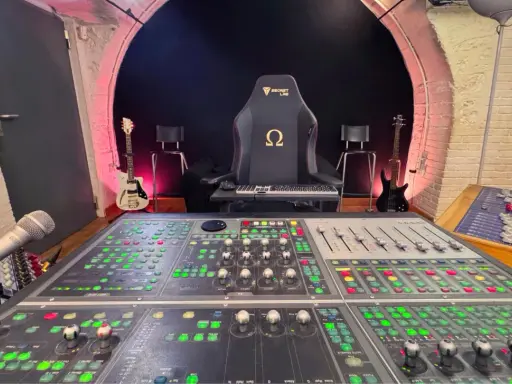 Console de mixage analogique dans un studio d'enregistrement, avec guitares et fauteuil de gamer.